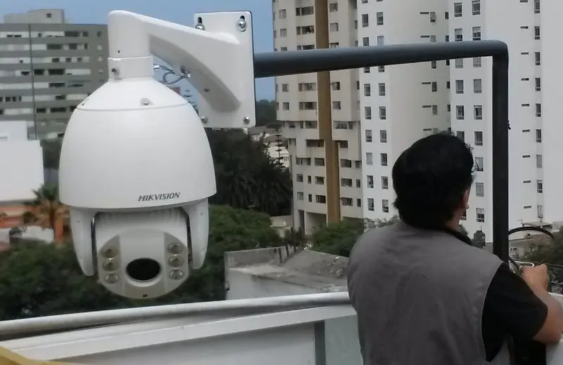 Cámara PTZ speed dome blanca instalada en soporte de pared en azotea de edificio en Lima, técnico realizando configuración inicial con edificios residenciales de fondo