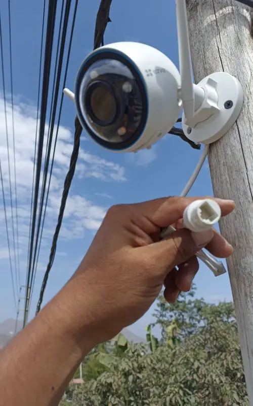 Técnico conectando cable de red a cámara WiFi exterior instalada en poste — instalación profesional en Lima
