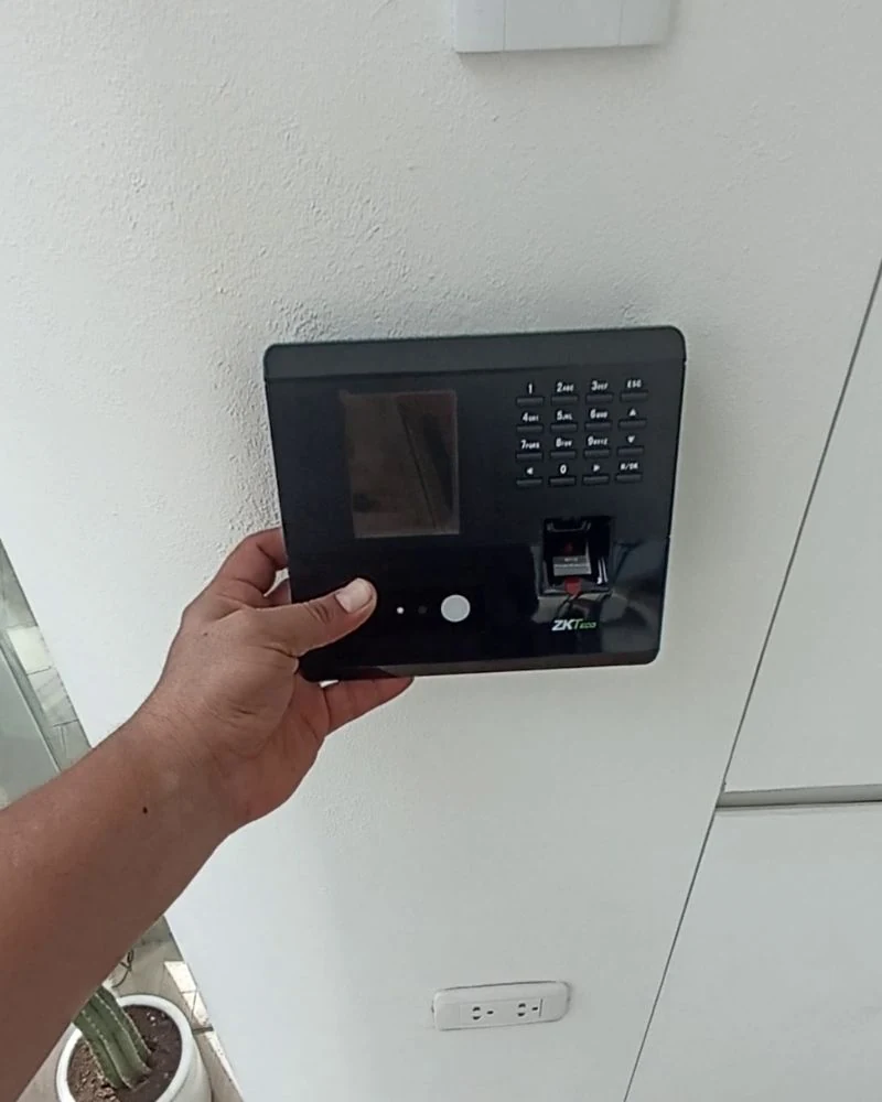 Técnico posicionando terminal biométrico de asistencia sobre soporte en pared de empresa peruana