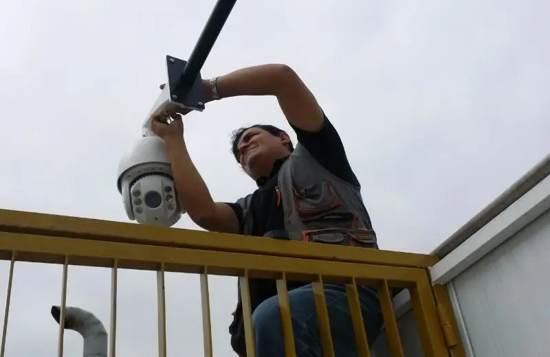 Técnico de Max Security Perú instalando cámara PTZ speed dome en soporte de poste metálico, vista desde abajo durante el montaje en Lima
